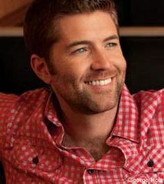 a man in a red and white checkered shirt smiles at the camera while sitting down