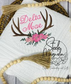 a white quilt with pink flowers and deer antlers on it next to a beaded necklace