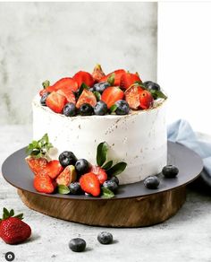 a white cake topped with berries and blueberries on top of a wooden platter