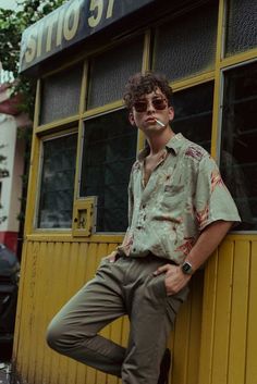 a man leaning on the side of a building with his hand on his hip while wearing sunglasses