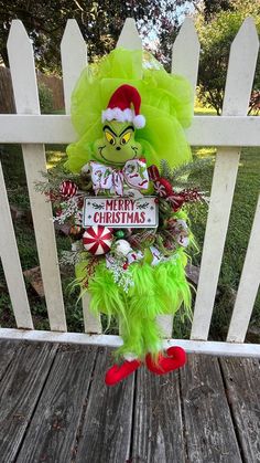 the grin face wreath is hanging on the front porch fence, decorated with green feathers and candy canes