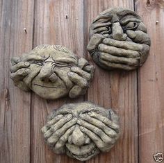 three clay faces are sitting on a wooden surface, one has eyes and the other has hands