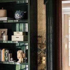 a green book shelf with books and vases on it