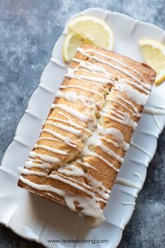 a loaf of lemon bread with icing on a white plate next to sliced lemons