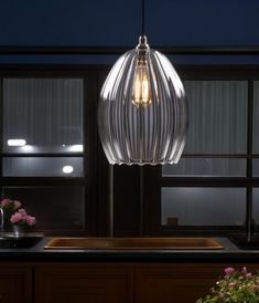 a light that is hanging over a sink in a kitchen with flowers on the counter