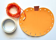 an orange piece of paper next to a spool of thread and some scissors on a white surface