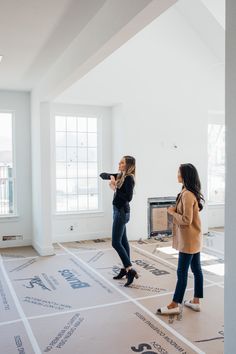 two women are standing in an empty room and one is pointing at something on the floor