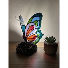 a colorful butterfly lamp sitting on top of a table next to a potted plant