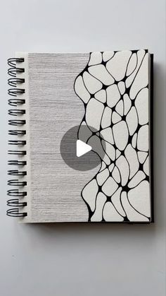 a spiral notebook with black and white designs on the cover, next to an apple logo