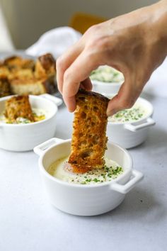 a person dipping something into some soup in small white bowls with other dishes behind them