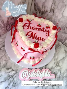 a heart shaped cake with the words twenty nine and cherries on it sitting on top of a marble counter