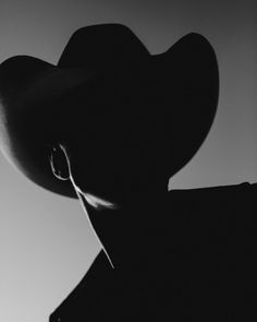 a black and white photo of a man wearing a cowboy's hat in the shadows