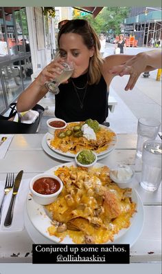 a woman sitting at a table with plates of food and drinks in front of her