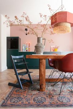 a dining room table with two chairs and a vase on top of it in front of a pink wall