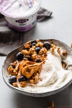 a bowl filled with yogurt and blueberries on top of a table next to a spoon