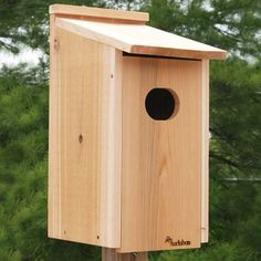 a wooden bird house on a post with trees in the background