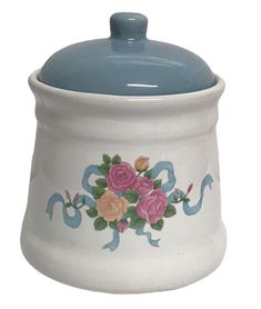 a blue and white ceramic sugar jar with flowers painted on the front, sitting on a white surface