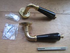 two brass and black handles on a wooden table next to some plastic bags with scissors