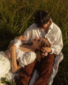 a man and woman laying in the grass with their arms around each other's shoulders