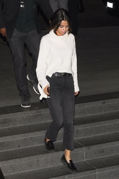 a woman walking down some steps wearing black pants and a white sweater with her hands in her pockets