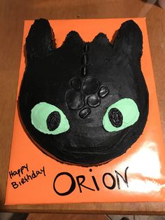 a black cat cake with green eyes on an orange plate that says happy birthday orion