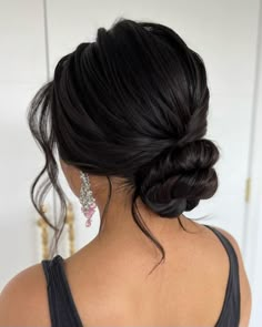 a woman with her hair in a low bun, wearing earrings and a black tank top