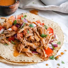 a tortilla with shredded meat and vegetables on it next to a bowl of sauce