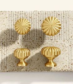 three golden knobs on a white wall in front of a beige and tan background