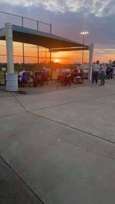 a group of people standing around in front of a building with the sun setting behind them