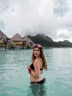 a woman is sitting in the water near some huts