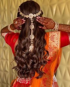 a woman with long brown hair wearing an orange and gold sari, holding her hands to her head