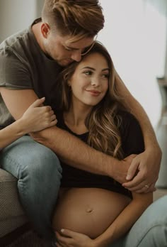 a pregnant couple cuddle while sitting on a couch