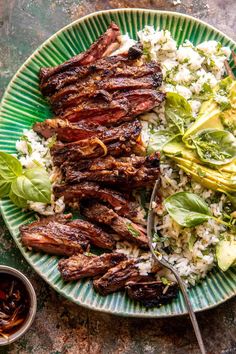 a plate with meat, rice and lettuce on it next to a spoon