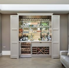 a wine bar with several bottles and glasses on the shelves, in front of a couch