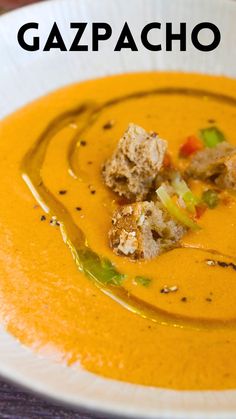 a white plate topped with soup and croutons on top of a wooden table