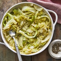 a white bowl filled with cabbage and some seasoning next to a spoon on top of a wooden table