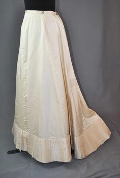 ANTIQUE BUSTLE SKIRT CANDLELIGHT SATIN 1890s A 1890's lovely candlelight satin bustle back full skirt in an off white beige color.  The bottom hemline is decorated with wide pleats in satin sweep. The back has hook and eye closures and additional hooks to attach to a bodice. Skirt has a off white cotton lining with a wide thick gauze fabric  at inner hem line at edge. Deaccessioned from the Strong museum of Rochester New York.  CONDITION: In very good wearable clean condition. with one small stain as shown in photo, and some splitting in bottom pleats on fold lines. MEASUREMENTS: Waist measures 28", length in back 46", length in front 39-1/2". The piece is well preserved and still worthy of collecting, displaying or wearing. Dates from the 1890's when these skirts were in great favor with Bustle Skirt, Fashion Organization, Gauze Fabric, Satin Skirt, White Beige, Full Skirt, Beige Color, Bodice, Womens Skirt