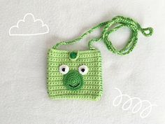 a crocheted bag with a green frog face on the front, and a white cloud in the background