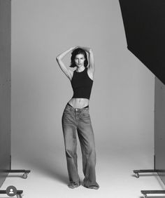 a black and white photo of a woman posing in front of a studio backdrop with her hands on her head