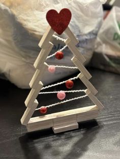 a christmas tree made out of wooden sticks and string with a red heart on top