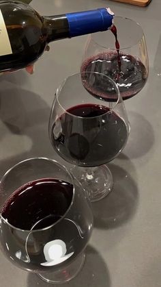 two wine glasses filled with red wine being poured into one glass and the other is empty