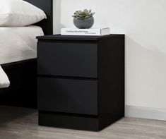 a black night stand with two drawers and a plant on it next to a bed