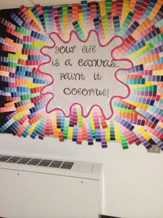 an art project is displayed on the wall above a computer screen with words written in rainbow colors