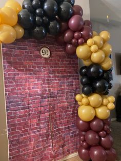 the balloon arch is decorated with black, yellow and grey balloons in front of a brick wall