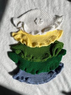 three crocheted hats are sitting next to each other on a white shirt,