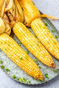 corn on the cob with green onions and garlic sitting on a plate next to an ear of corn