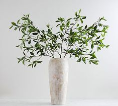 a white vase filled with green leaves on top of a marble table next to a wall