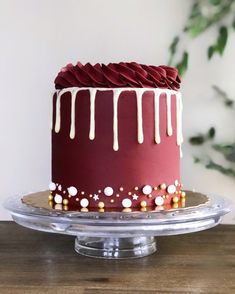 a red cake with white icing and gold sprinkles on a clear plate