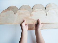 someone is holding up a wooden cloud on the wall above their head, with one hand reaching for it