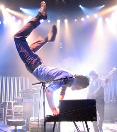 a man doing a handstand on top of a keyboard in front of stage lights